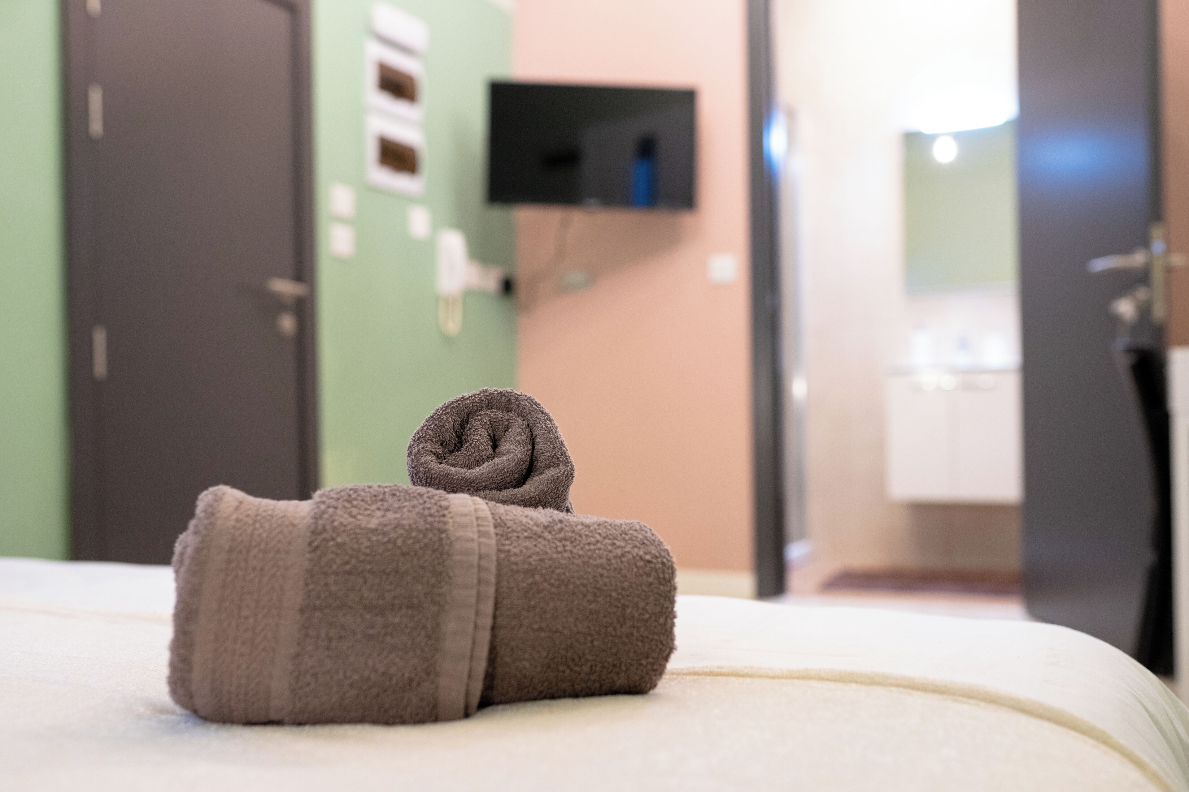 A neatly made bed with two rolled towels in a hotel room.