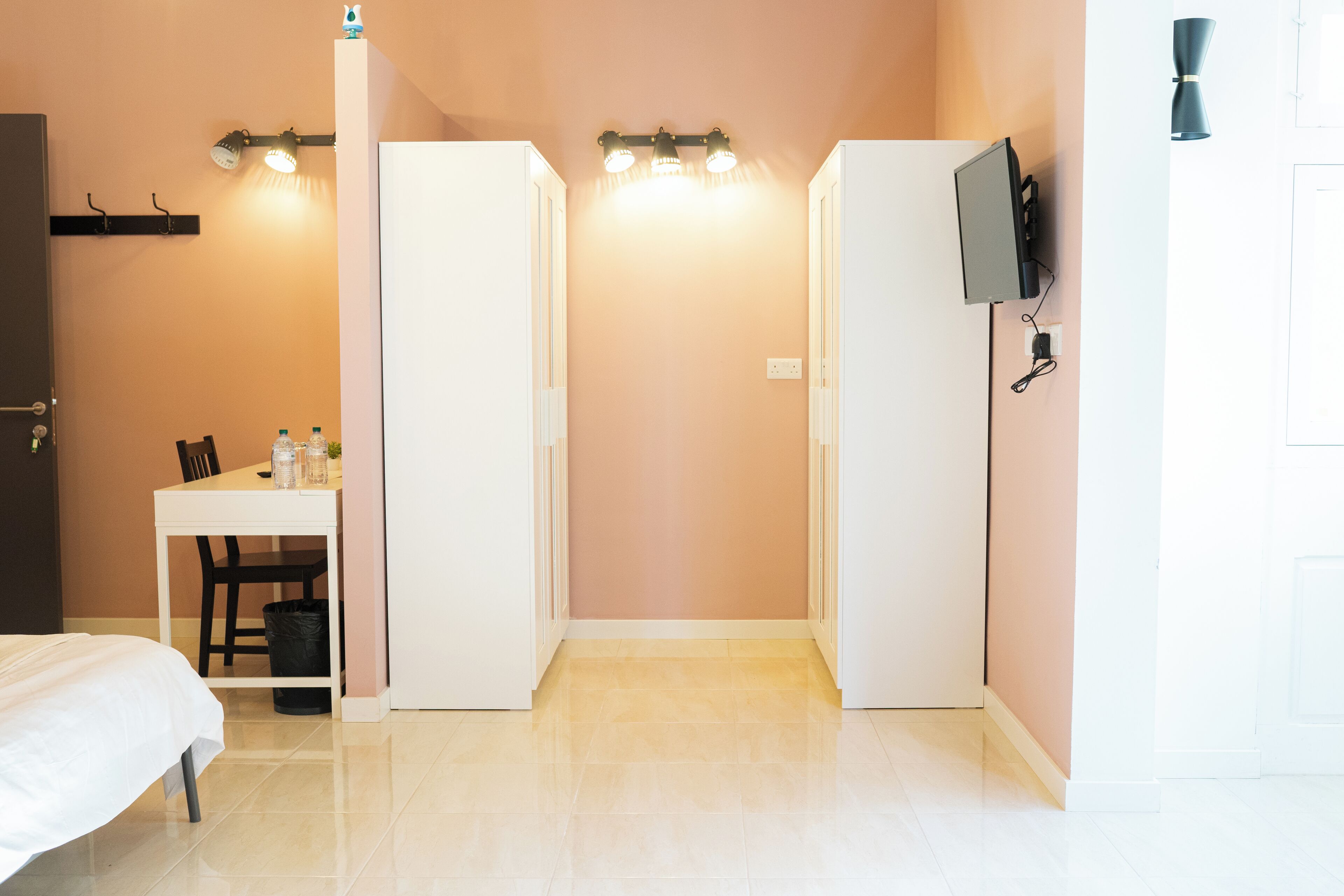 A hotel room with a bed, a desk with chairs, a trash bin, and a TV mounted on the wall.