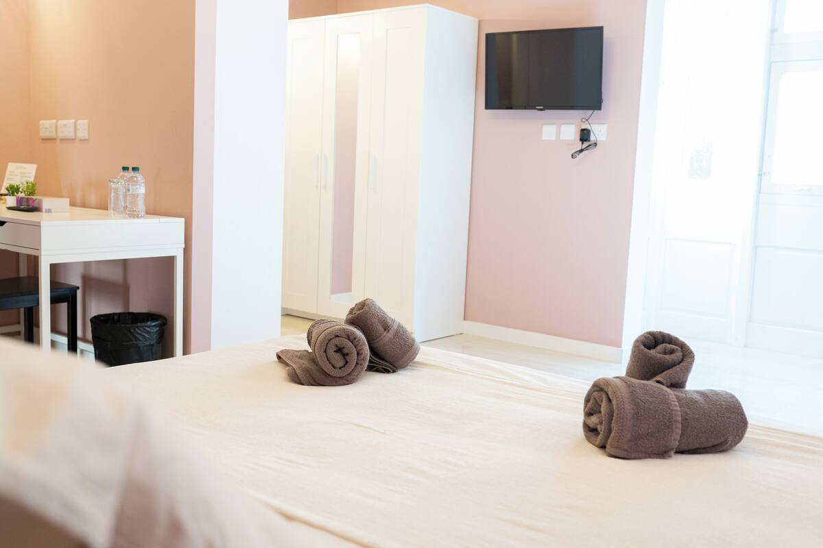 A hotel room with a bed, a desk, a TV mounted on the wall, and a window.