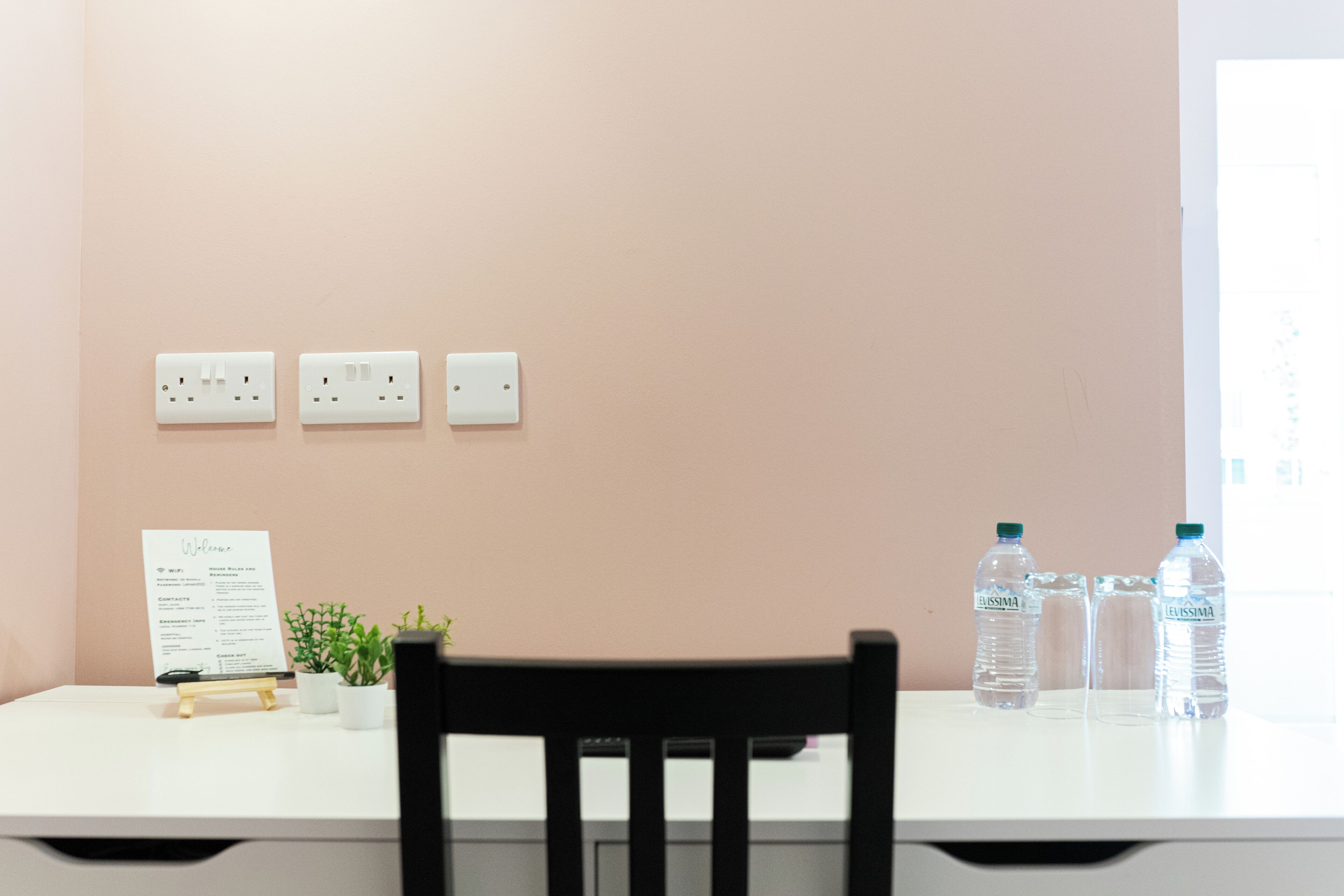 Un bureau avec une chaise, une plante en pot, une pancarte de bienvenue et deux bouteilles d’eau.