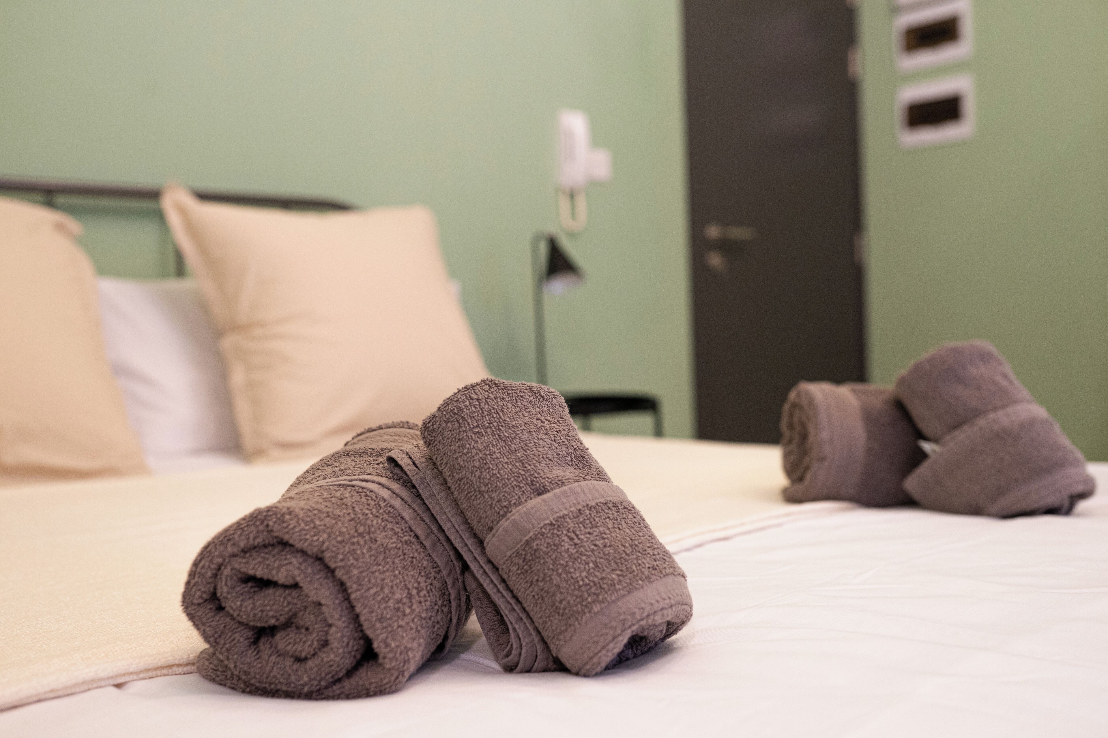 A neatly made bed with rolled towels and a lamp in a room with green walls and a door.