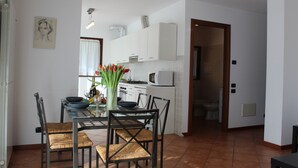 A dining area with a table set for four, surrounded by wicker chairs. A vase with flowers is on the table. - Rosemary 1 apartment in Agra with pool (Agra)
