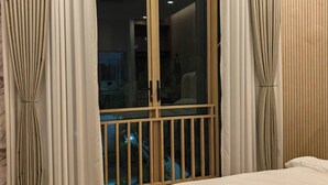 Un dormitorio con una cama grande, una puerta corrediza de vidrio con cortinas y piso de madera.