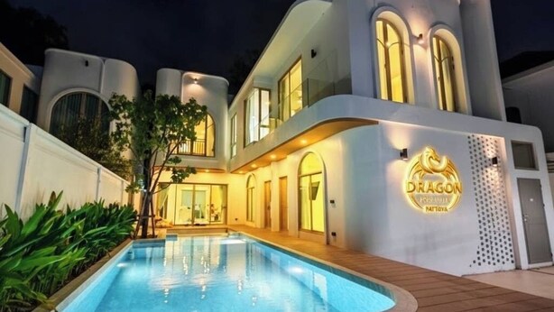 Una casa moderna de dos pisos con piscina, exterior bien iluminado y un logotipo en el lateral.