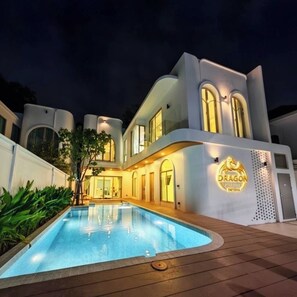 Uma casa moderna de dois andares com piscina, fachada bem iluminada e um logotipo lateral.