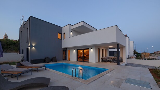 Ein modernes Haus mit Swimmingpool, Sitzgelegenheiten im Freien und einer überdachten Terrasse.