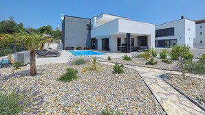 Ein modernes, zweistöckiges Haus mit Swimmingpool, umgeben von einem angelegten Garten mit verschiedenen Pflanzen und einem Kiesweg.