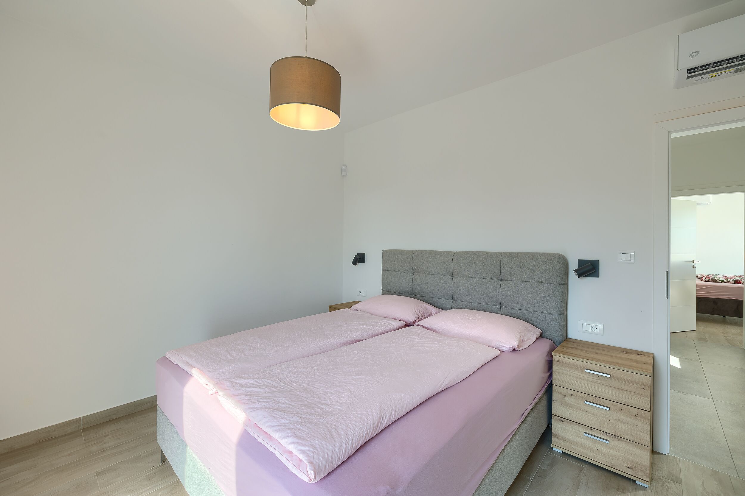 Um quarto com uma cama, mesa de cabeceira, guarda-roupa e luminária pendente.