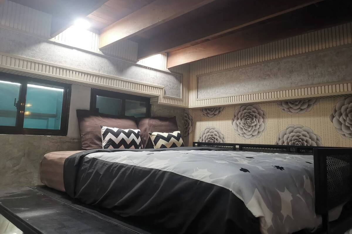 Een slaapkamer met een bed, kussens, een raam en decoratieve wandbekleding.