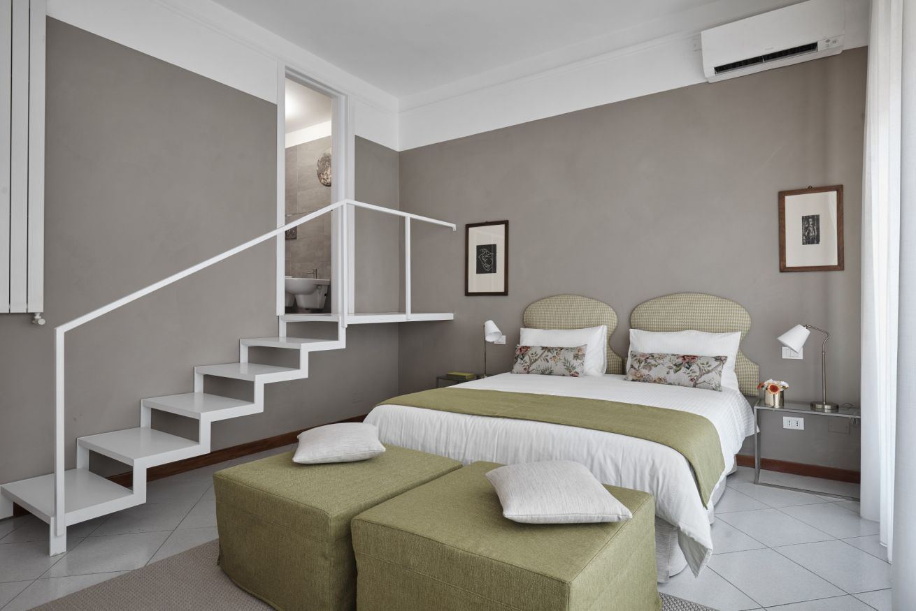 A bedroom with a staircase, a bed with two pillows, a nightstand, and a wall-mounted air conditioner.