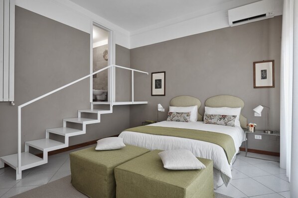 A bedroom with a staircase, a bed with two pillows, a nightstand, and a wall-mounted air conditioner.