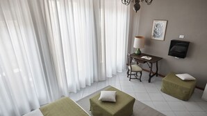 A hotel room with a bed, two ottomans, a desk with a lamp, a chair, and a television on the wall. - Green H- Earth Suite for 2 persons (Florence)