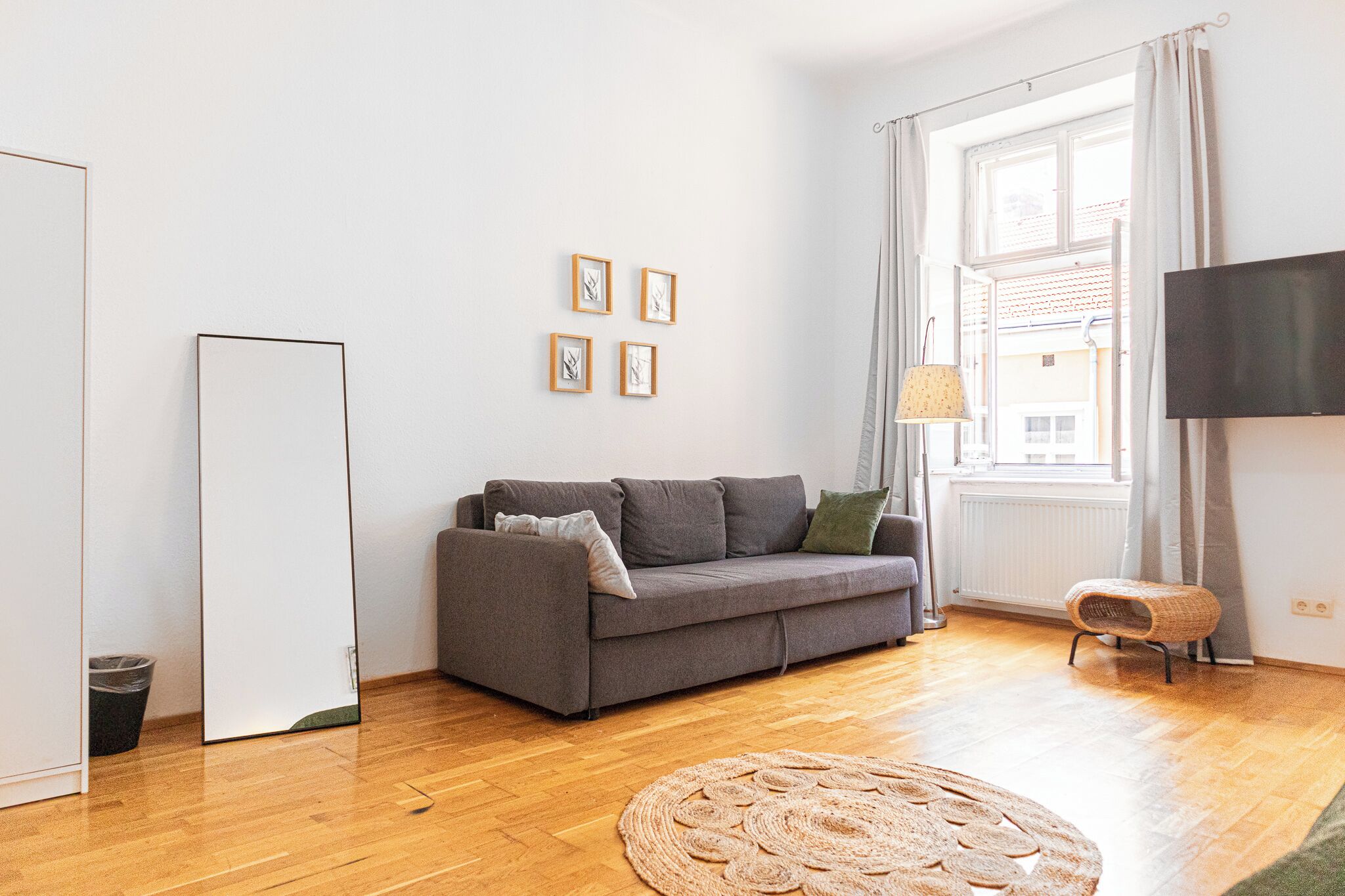 A modern living room with a grey sofa, a round woven rug, and a flat-screen TV mounted on the wall.