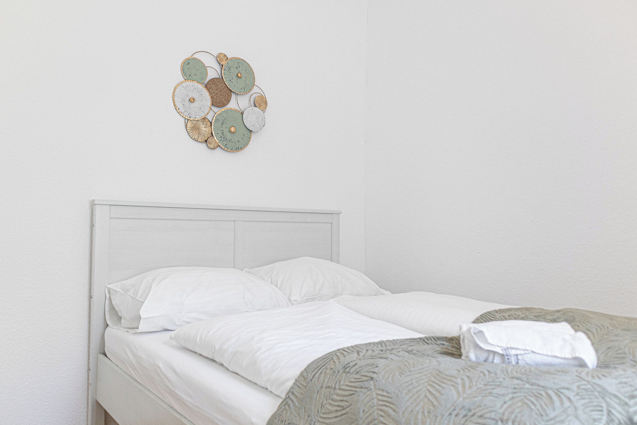 Una cama bien tendida con sábanas blancas y un adorno decorativo en la pared de arriba.
