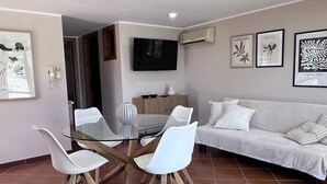 A modern living room with a glass dining table, white chairs, a sofa, and artwork on the walls. - Villa Romy with shared pool and garden - My Rental Homes (Castellammare Del Golfo)