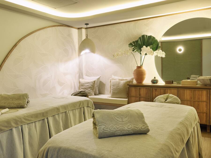 Une salle de spa équipée de deux lits, d’un grand miroir, d’une armoire en bois et d’un vase rempli de fleurs.