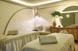 Un cuarto de spa con dos camas, un espejo grande, un armario de madera y un jarrón con flores.