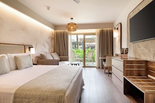 Habitación de hotel con cama, escritorio, silla, televisor y vistas al exterior.