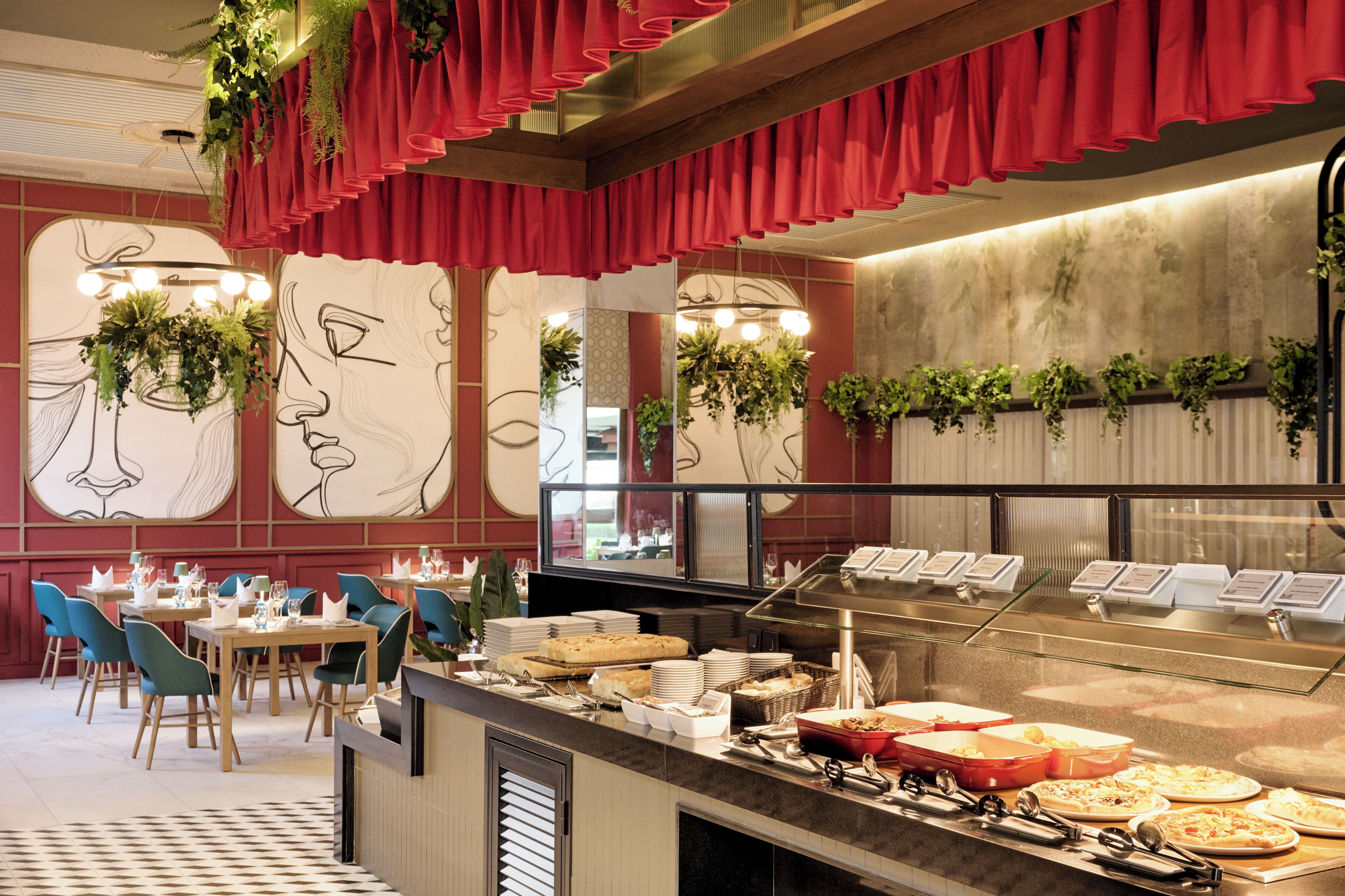 A buffet area with a variety of food options, including pizzas and salads, in a modern restaurant setting with red curtains and wall art.