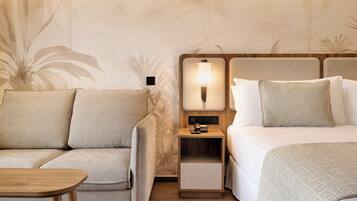 A hotel room with a sofa, a bed, a nightstand with a lamp, and a wooden table.