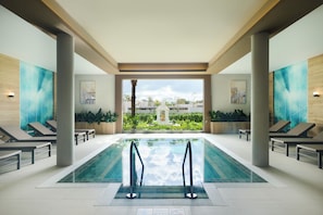 Ein moderner, überdachter Pool mit Liegestühlen und Blick auf einen angelegten Garten.