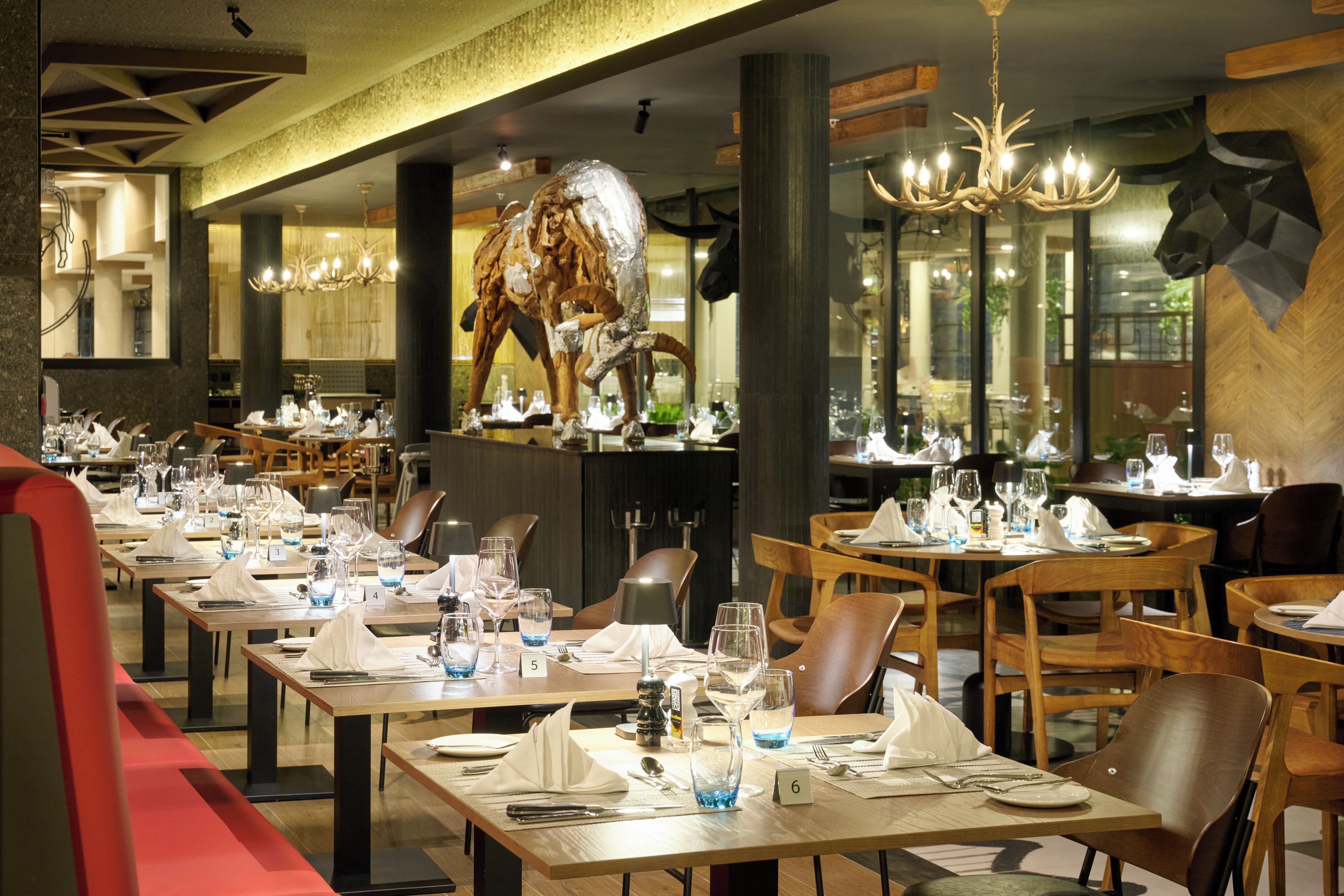 A restaurant with multiple dining tables, chairs, and a large decorative sculpture.