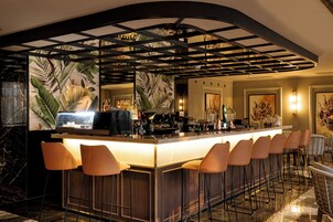 Una zona de bar con una barra larga, varios taburetes y un techo decorativo.