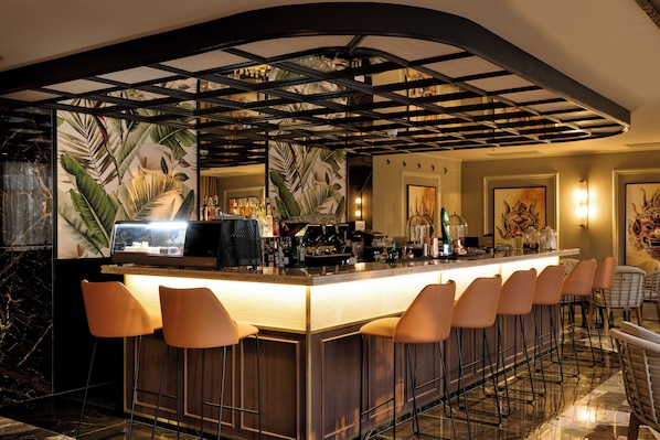 Una zona de bar con una barra larga, varios taburetes y un techo decorativo.