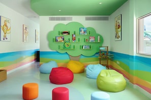Uma sala de brinquedos infantil com sacos de poltrona coloridos, uma estante em formato de árvore verde e brinquedos educativos.