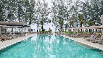 A pool area with lounge chairs and umbrellas, surrounded by trees and a view of the sea.