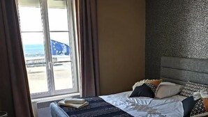Een slaapkamer met een bed, uitzicht op zee door een raam, en een behang met een patroon.