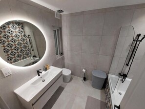 A modern bathroom with a large mirror, a sink, a toilet, and a shower area. - Modern 3BR Apt With Large Balcony (Marsalforn)