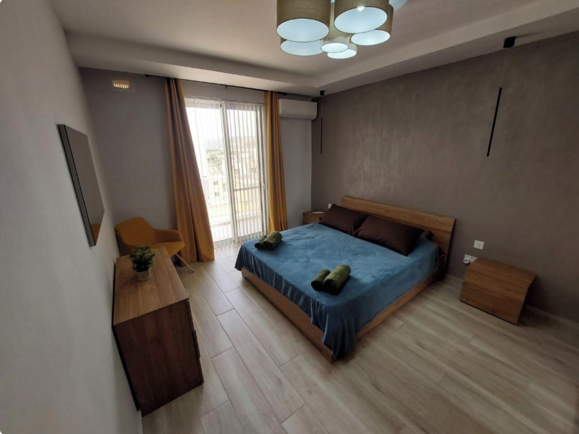 A modern bedroom with a large bed, a wooden desk, and a chair.