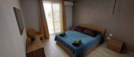 A modern bedroom with a large bed, a wooden desk, and a chair.