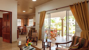 A spacious living area with a dining set, a sofa, and a balcony with a view of the garden.