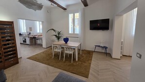 A modern living room with a dining area, a TV mounted on the wall, and a kitchen in the background. - Ganaceto100   Blu apartment   MW Collection (Modena)
