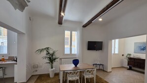 A spacious living room with a wooden dining table, white chairs, a large potted plant, and a TV mounted on the wall. - Ganaceto100   Blu apartment   MW Collection (Modena)
