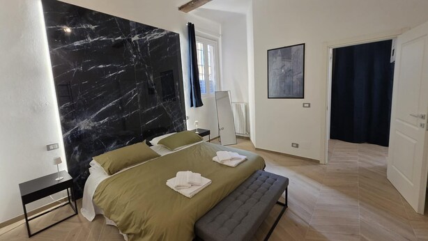 A modern bedroom with a large black marble wall, a bed with green bedding, a bench, and a door leading to another room. - Ganaceto100   Blu apartment   MW Collection (Modena)
