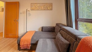 Ein modernes Wohnzimmer mit Ecksofa, Holztür, Stehlampe und einem fenster mit Vorhängen.