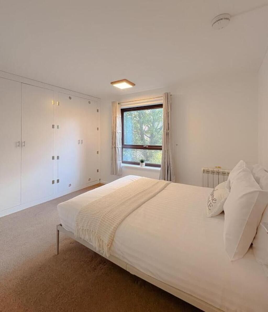 Een slaapkamer met een groot bed, een kledingkast en een raam met gordijnen.