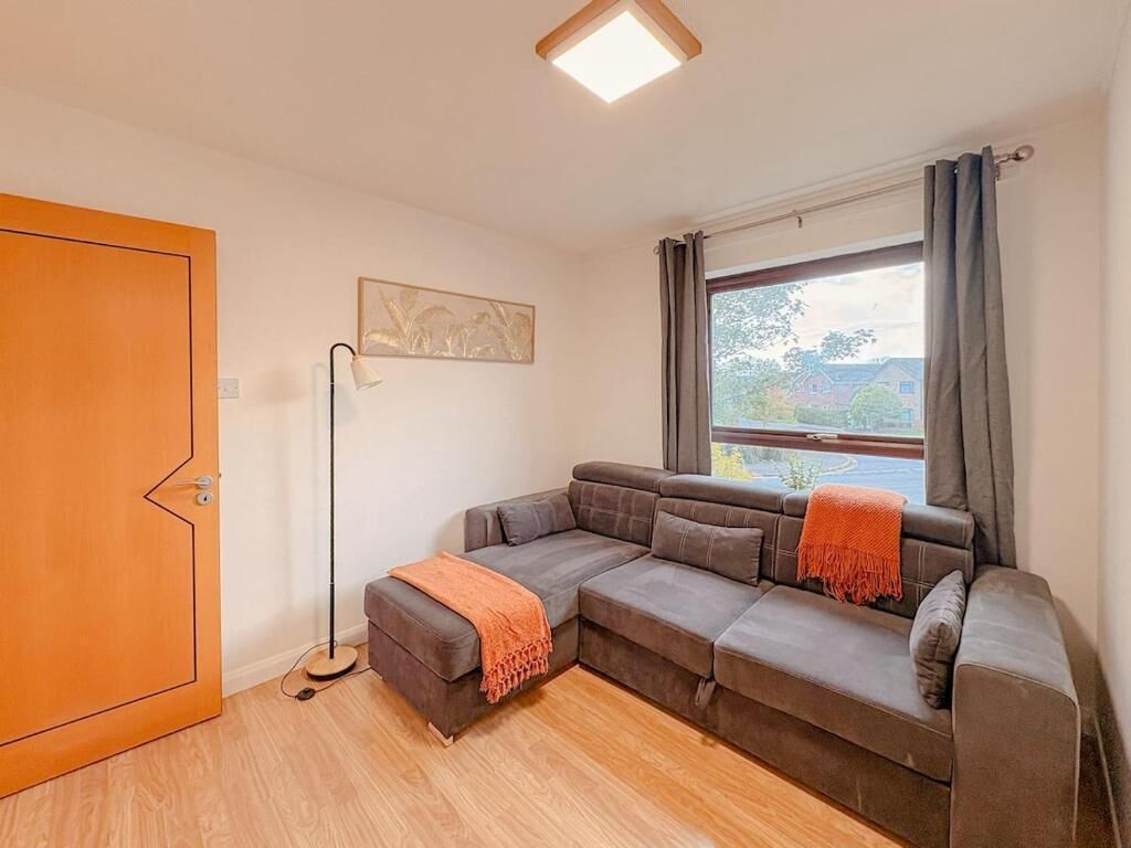 Un salon moderne avec un canapé d’angle, une lampe sur pied et une grande fenêtre agrémentée de rideaux.