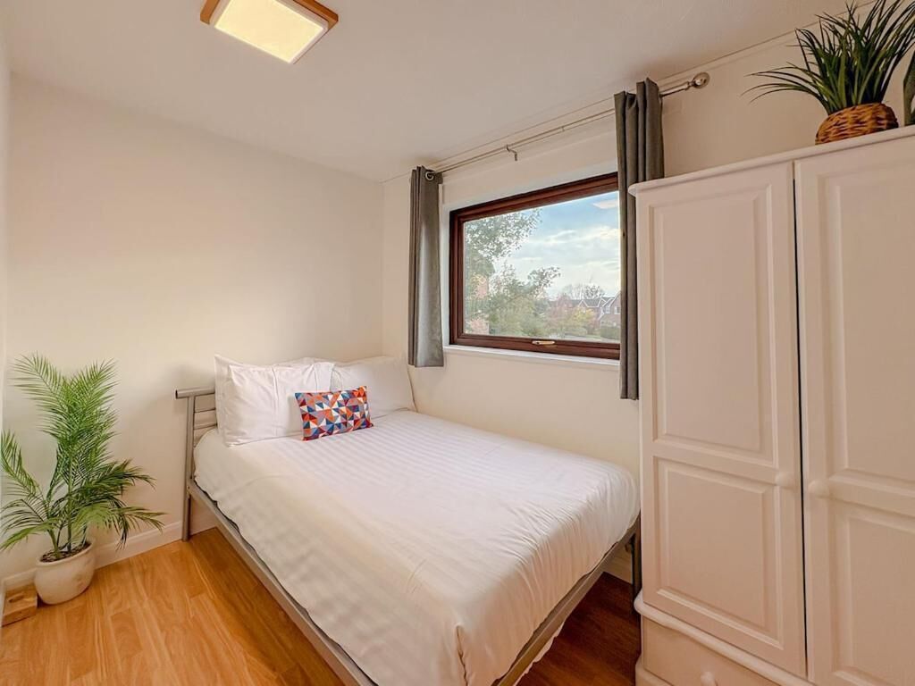 A bedroom with a bed, a window, a wardrobe, and a potted plant.