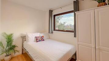 A bedroom with a bed, a window, a wardrobe, and a potted plant.