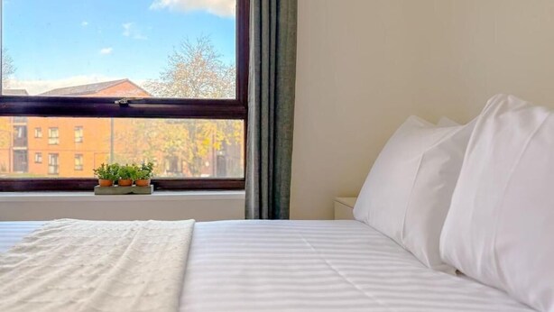 Ein Hotelzimmer mit einem Bett, einem Fenster mit Vorhängen und Blick auf Gebäude und Bäume.