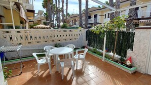 Une terrasse avec une table ronde et des chaises, un barbecue et un mur décoratif.