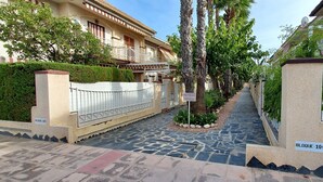 Un étroit sentier bordé de bâtiments dotés de balcons, une allée dallée de pierres et une clôture blanche.