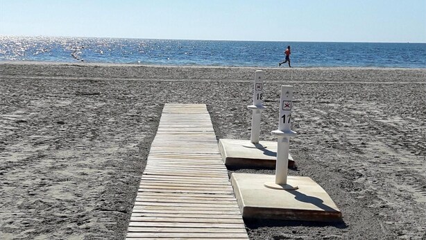 Un sentier en bois mène à une plage où se dressent deux piliers blancs, chacun portant un numéro.
