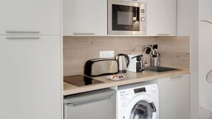 A modern kitchen with a microwave, toaster, kettle, and washing machine. - Appartements rue Garnier (Neuilly-sur-Seine)