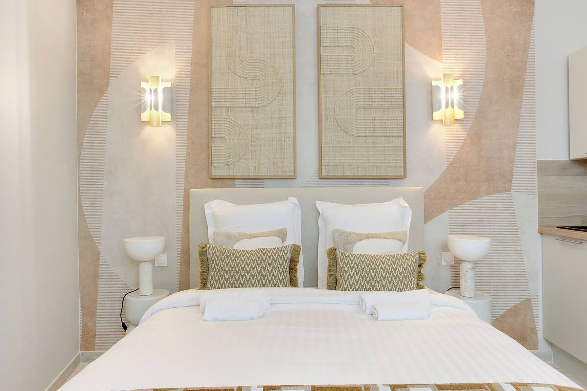A modern hotel room with a large bed, two wall-mounted light fixtures, and decorative wall panels.