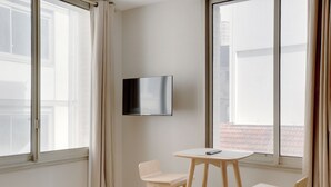 A room with two wooden chairs, a small table, and a mounted TV. - Appartements rue Garnier (Neuilly-sur-Seine)